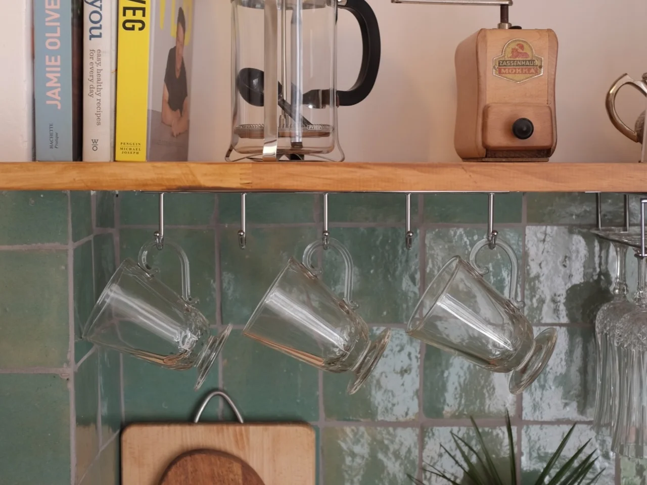 French press and hand grinder on an oak shelf above green zellige tile