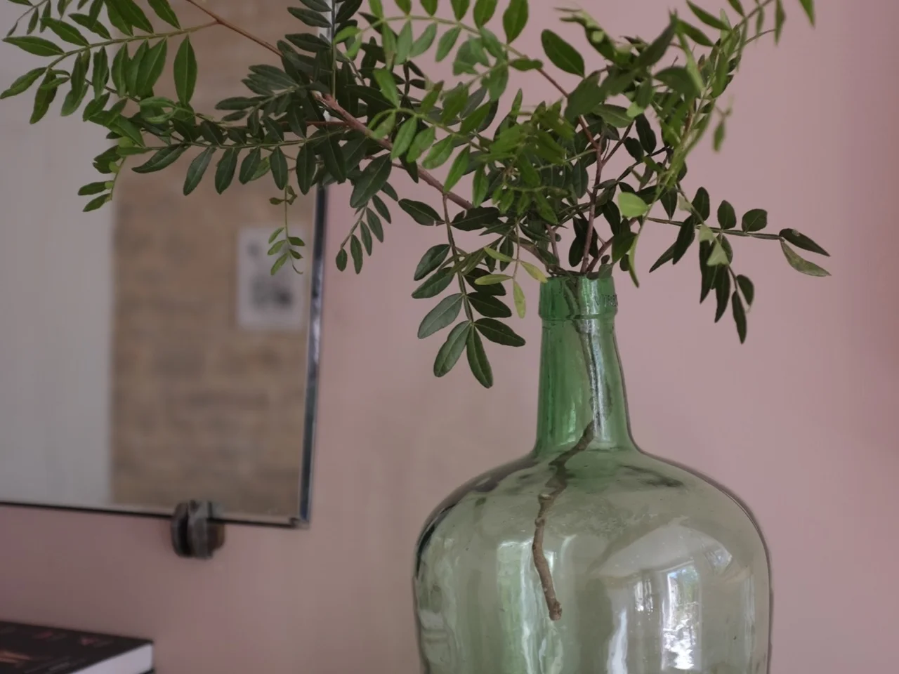 Green glass demijohn holding garden cuttings on a pink mantel