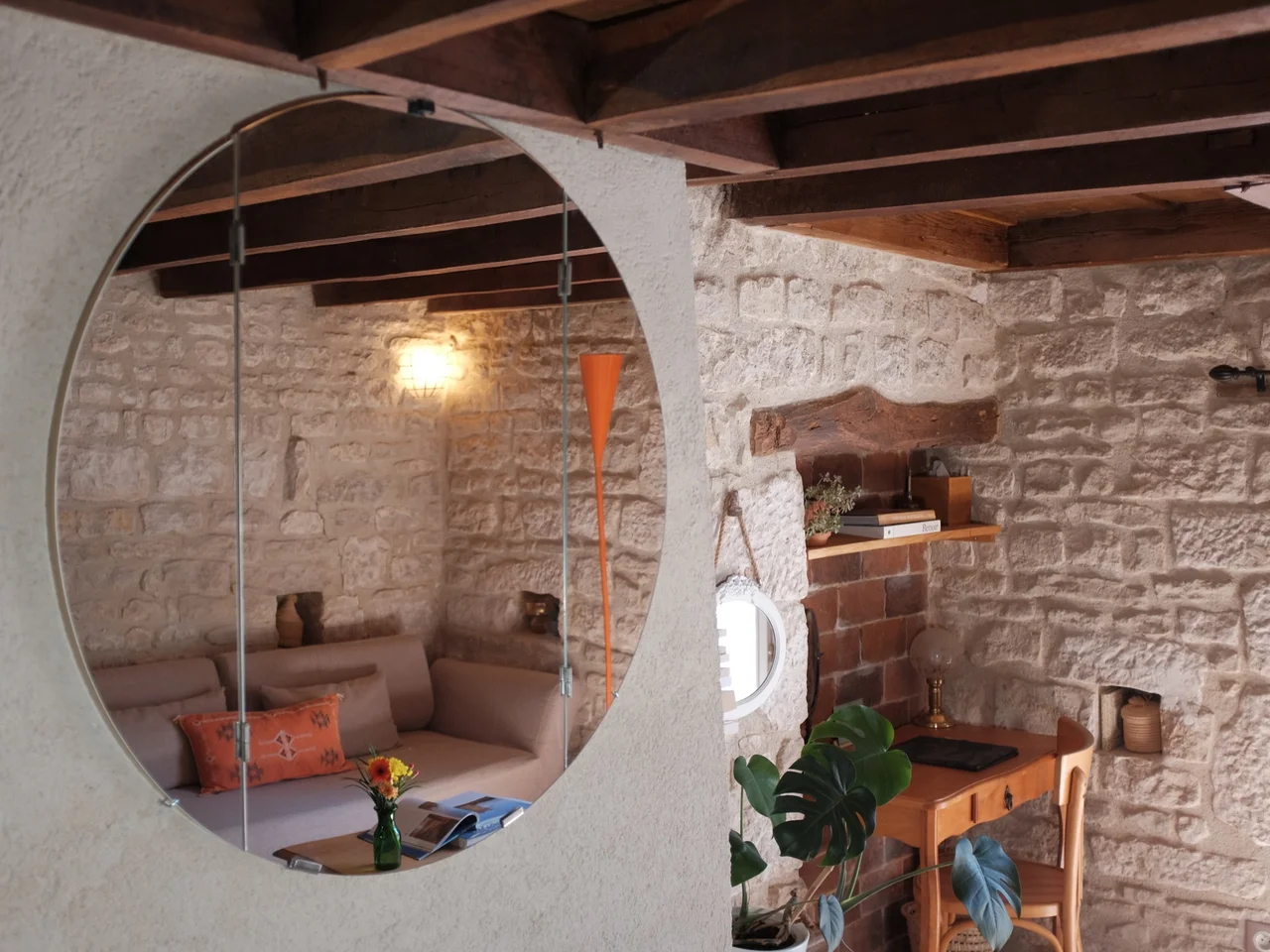 Round mirror reflecting the sitting corner and exposed beams