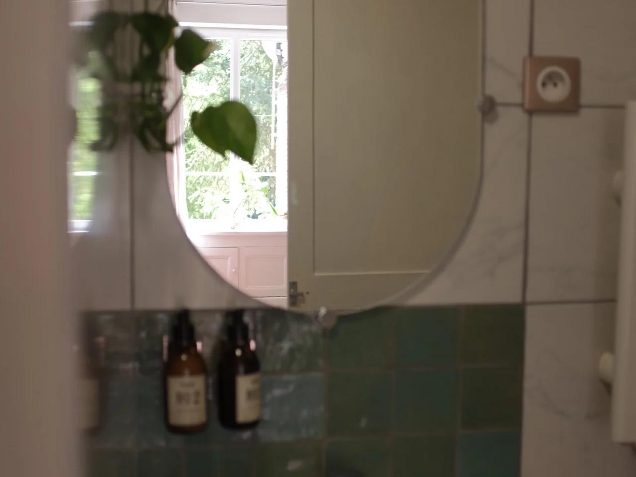 Bathroom basin and oval mirror with green zellige tile and open window