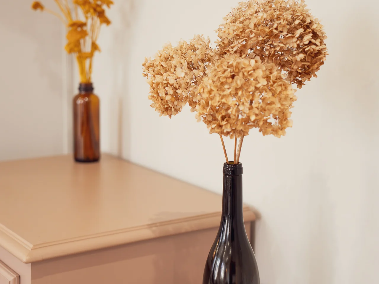 Dried hydrangeas in amber bottles on mauve dresser